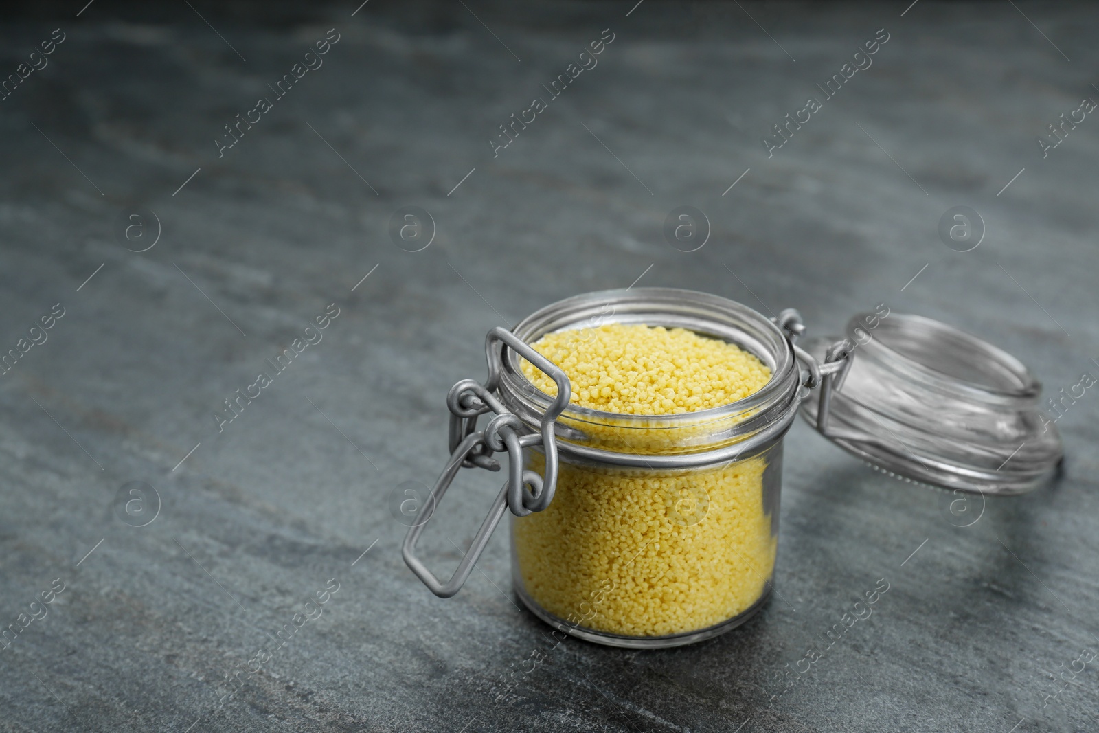 Photo of Glass jar of raw couscous on grey table. Space for text