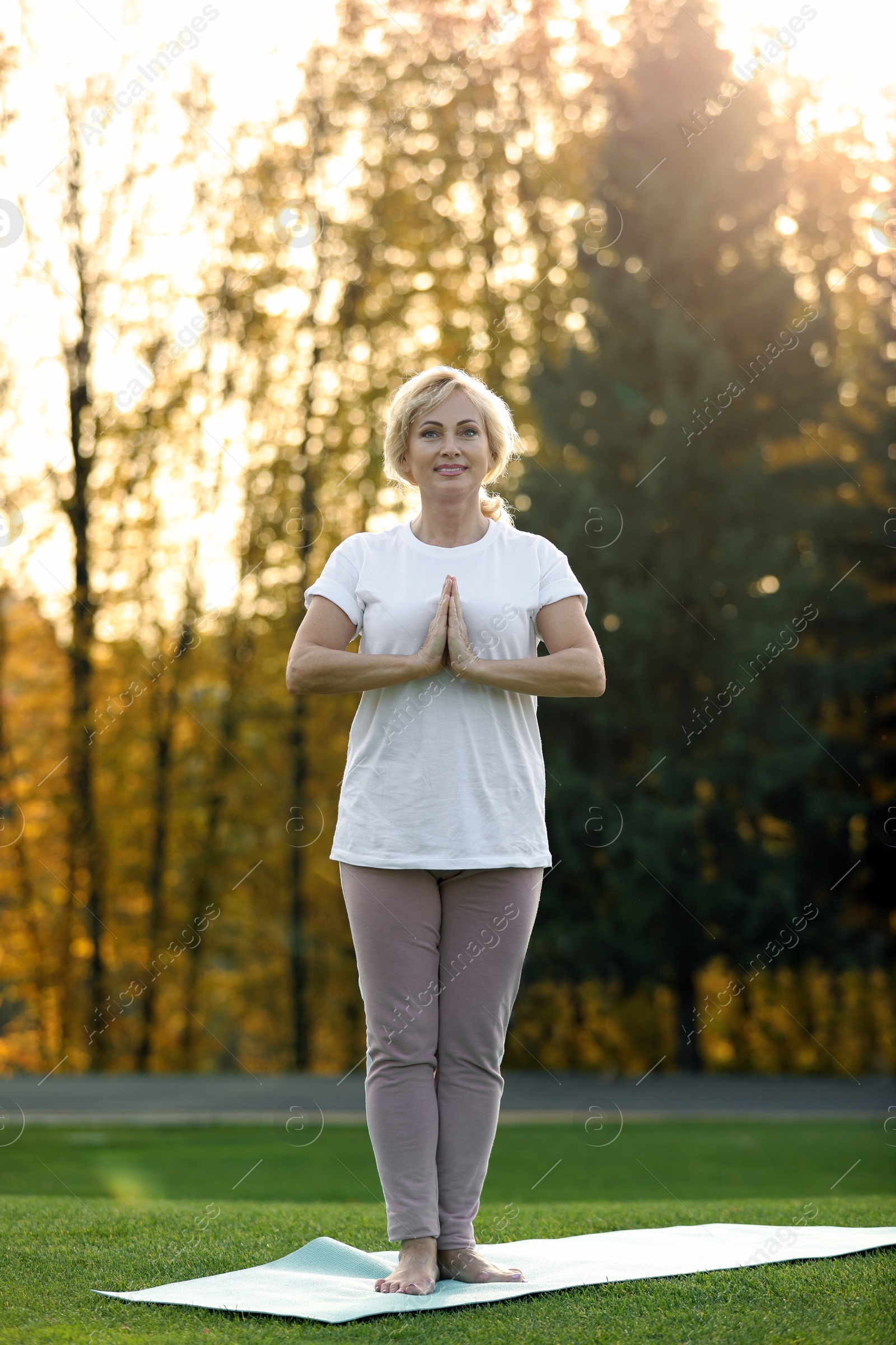 Image of Mature woman practicing yoga on green grass in park