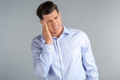 Young man suffering from headache on grey background