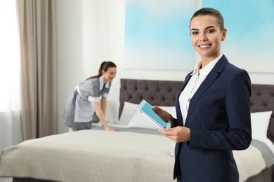 Photo of Housekeeping manager with tablet checking maid work in hotel room. Space for text