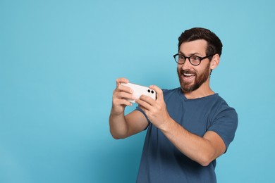 Emotional man playing game on smartphone against light blue background. Space for text