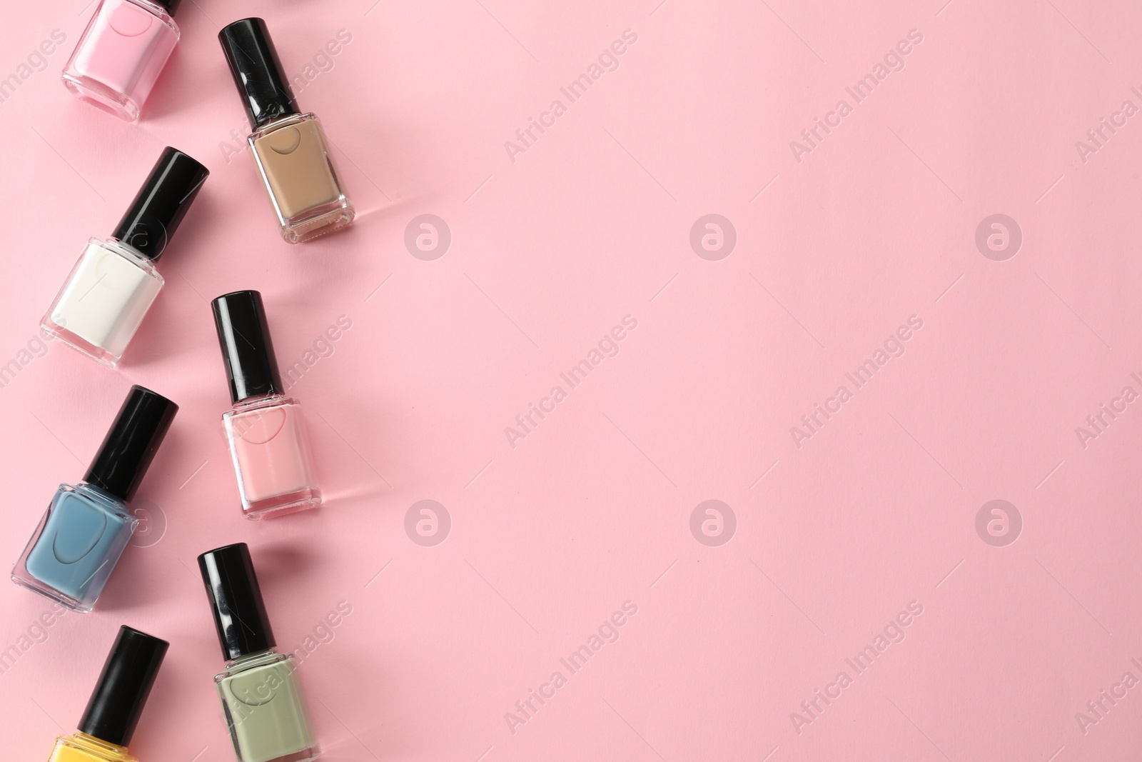 Photo of Pastel nail polishes in bottles on pink background, flat lay. Space for text