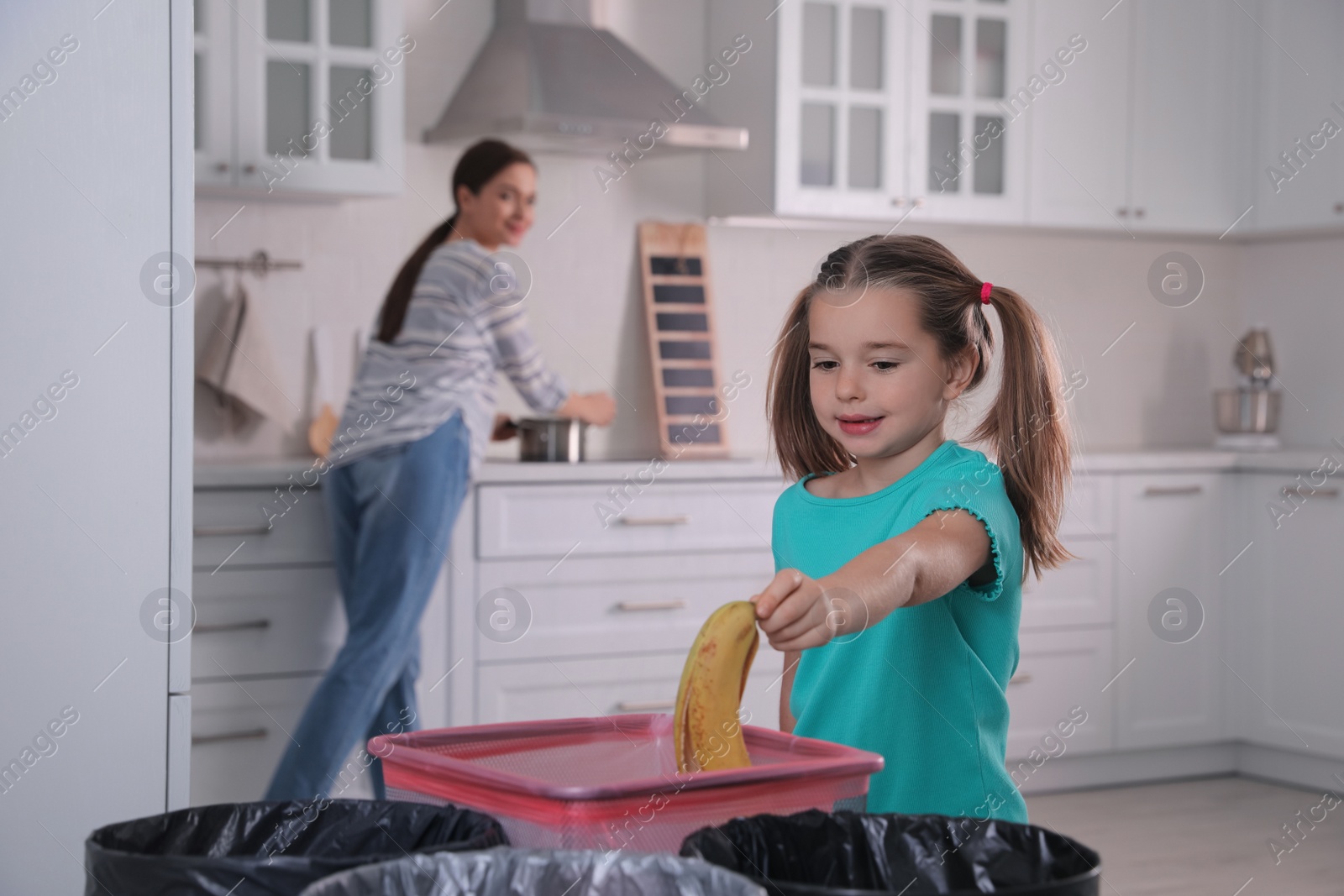 Photo of Little girl throwing banana peel into trash bin in kitchen. Separate waste collection