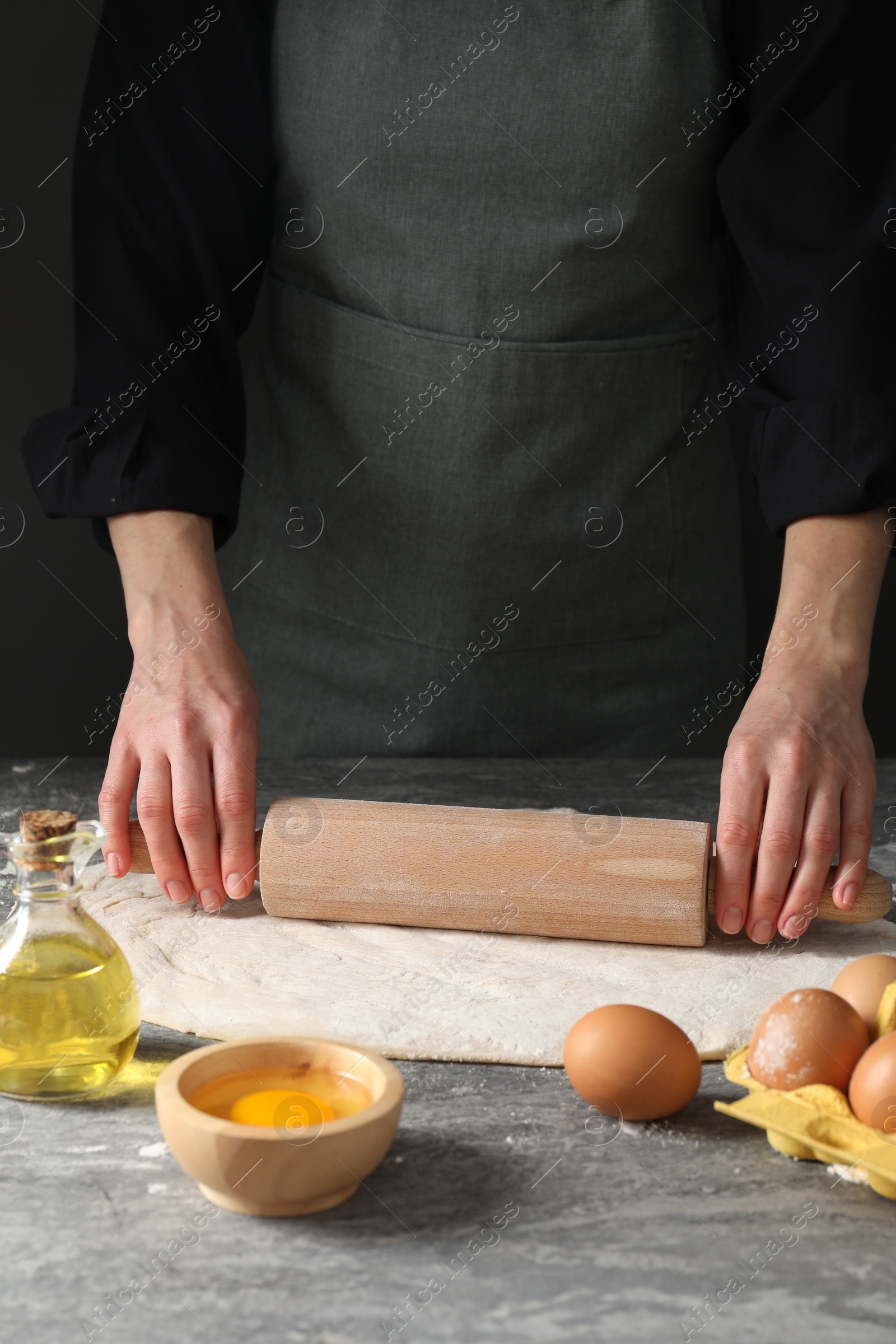 Photo of Woman rolling raw dough at grey table, closeup