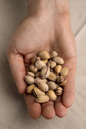 Photo of Woman holding tasty roasted pistachio nuts at table, top view