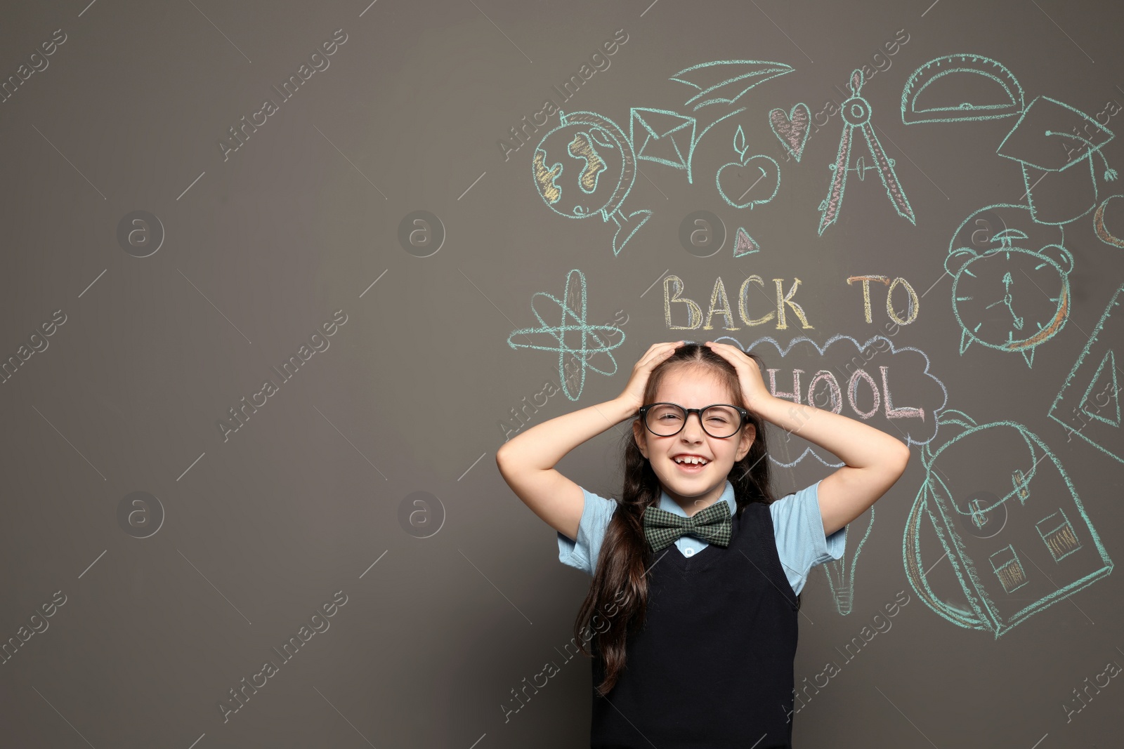 Photo of Little child in uniform near drawings with text BACK TO SCHOOL on grey background