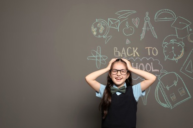 Little child in uniform near drawings with text BACK TO SCHOOL on grey background