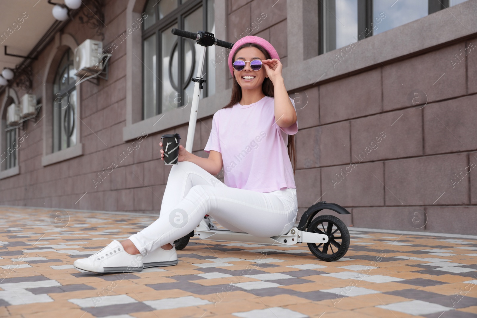 Photo of Young woman with cup of coffee sitting on electric kick scooter outdoors