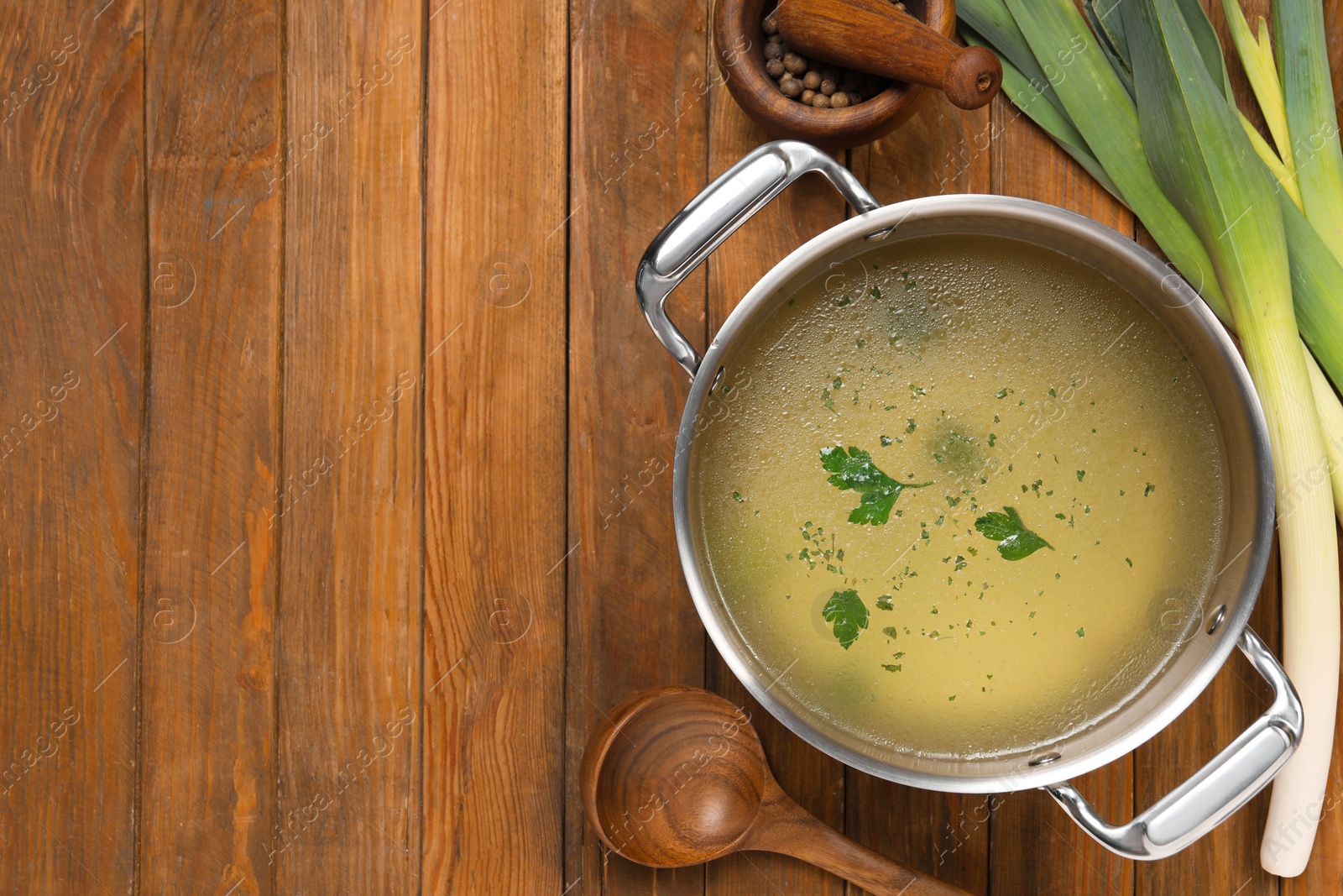 Photo of Pot with tasty bouillon, celery and peppercorn on wooden table, flat lay. Space for text