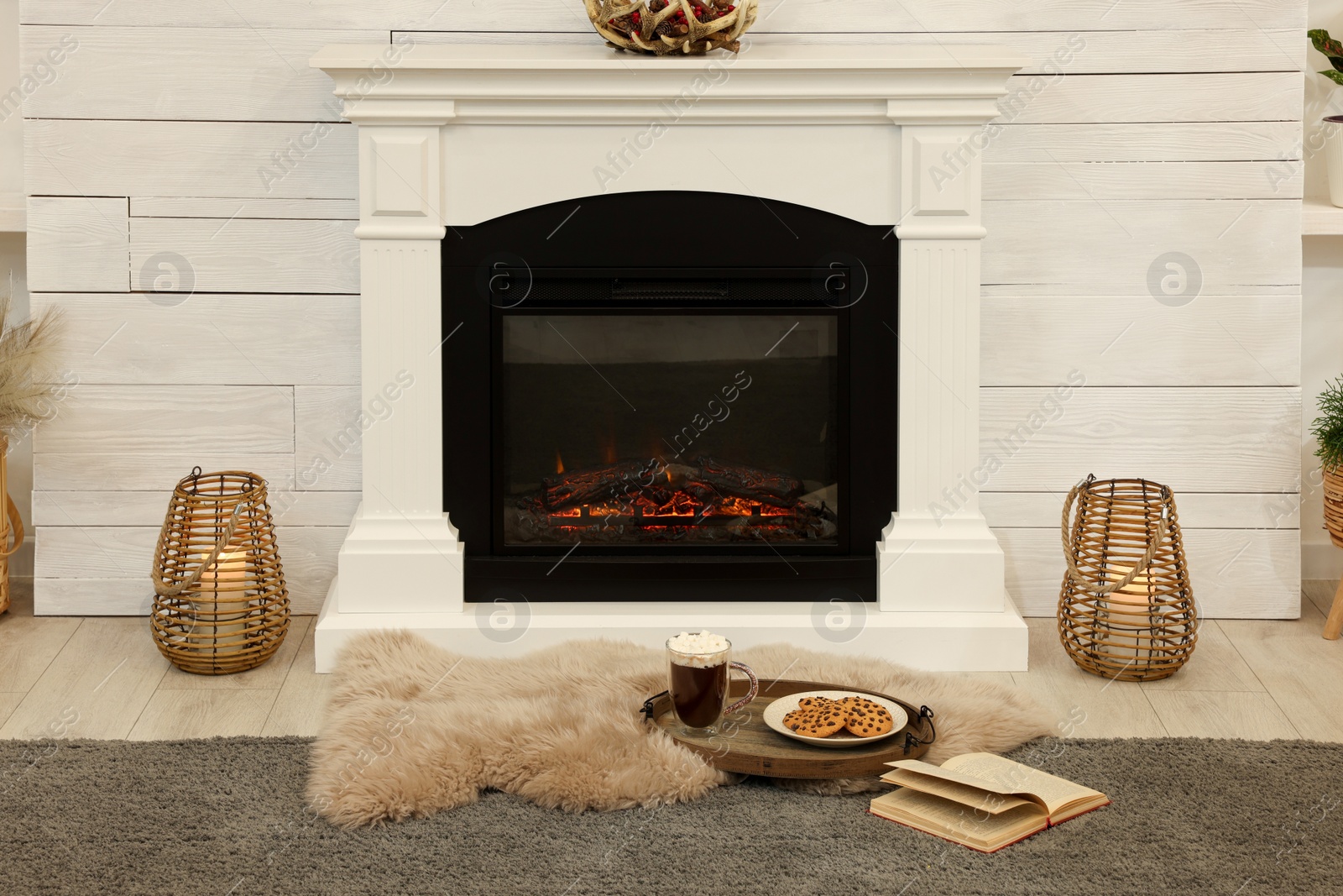 Photo of Open book, hot drink and cookies near decorative fireplace in living room. Cozy home atmosphere