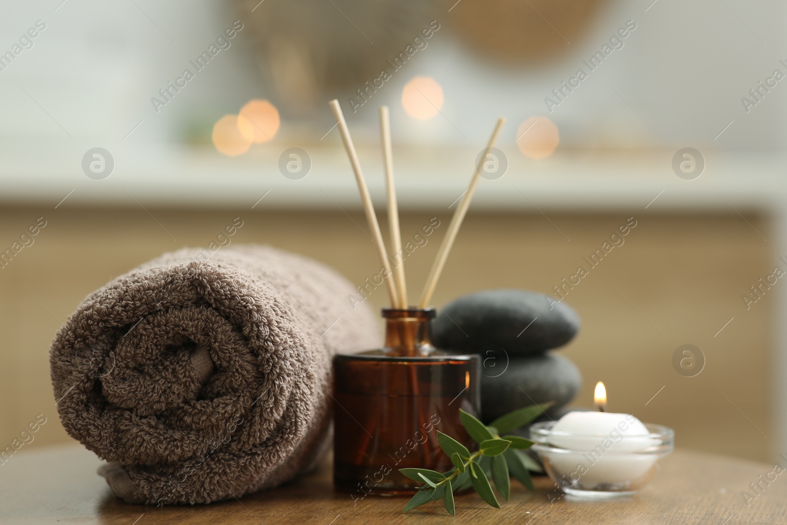 Photo of Spa composition. Rolled towel, aroma diffuser, massage stones and burning candle on wooden table indoors, closeup