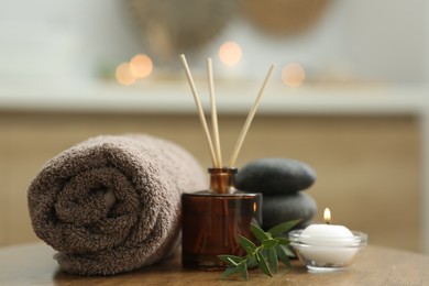 Spa composition. Rolled towel, aroma diffuser, massage stones and burning candle on wooden table indoors, closeup