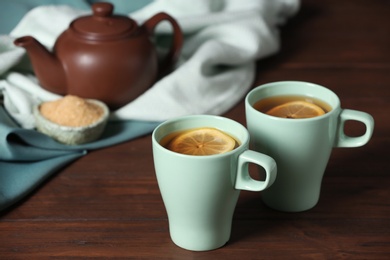 Photo of Cups of tea with lemon on wooden table. Space for text