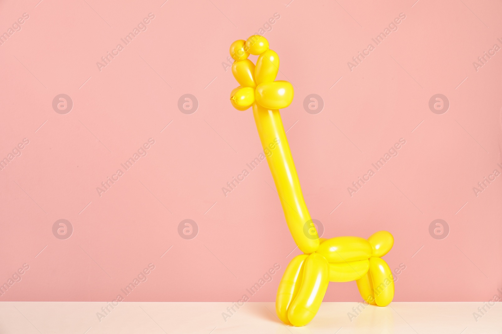 Photo of Giraffe figure made of modelling balloon on table against color background. Space for text