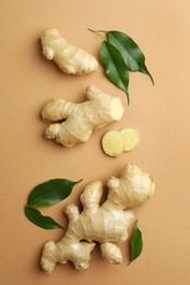 Photo of Fresh ginger with green leaves on light pale brown background, flat lay