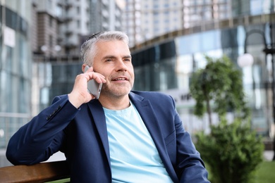 Photo of Portrait of handsome mature man talking on phone in city center. Space for text