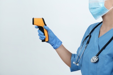 Photo of Doctor with infrared thermometer on light background, closeup. Checking temperature during Covid-19 pandemic