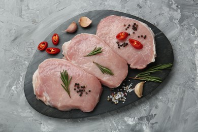 Photo of Pieces of raw pork meat, chili pepper and spices on grey textured table, top view