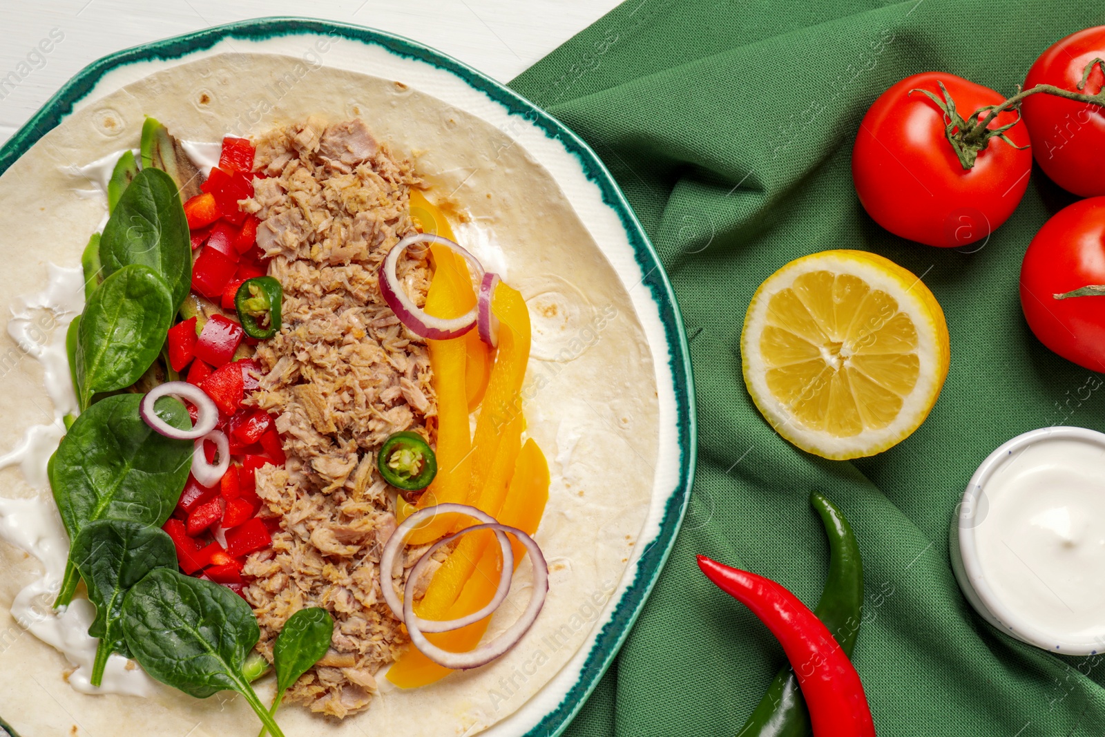 Photo of Delicious tortilla with tuna and vegetables on white table, flat lay. Cooking shawarma