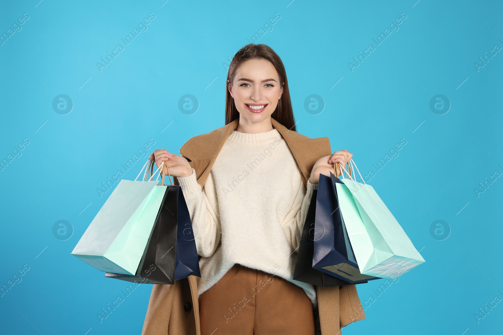 Photo of Happy young woman with shopping bags on light blue background. Big sale