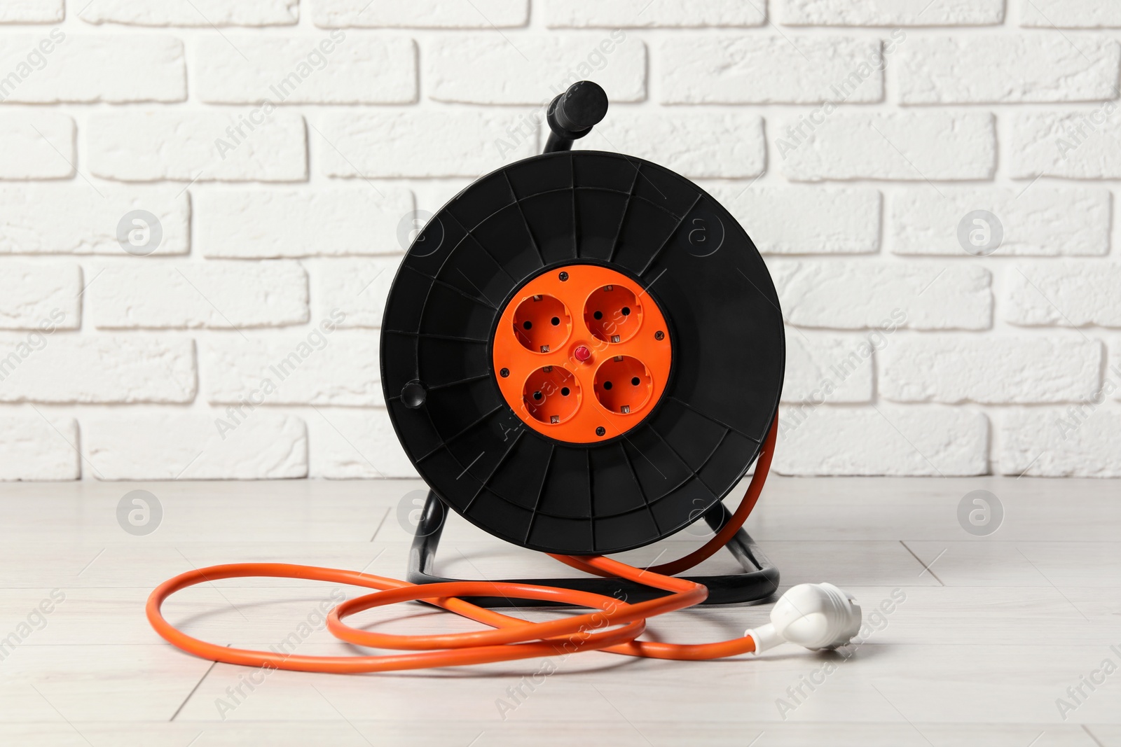 Photo of Extension cord reel on floor near white brick wall. Electrician's equipment