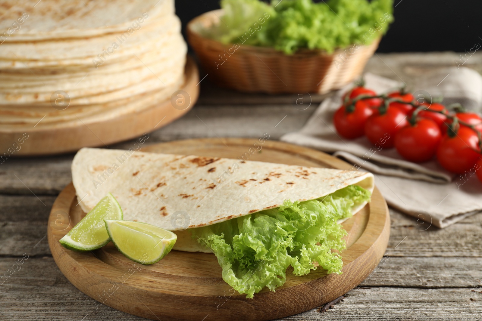 Photo of Tasty homemade tortillas, lettuce, lime and tomatoes on wooden table