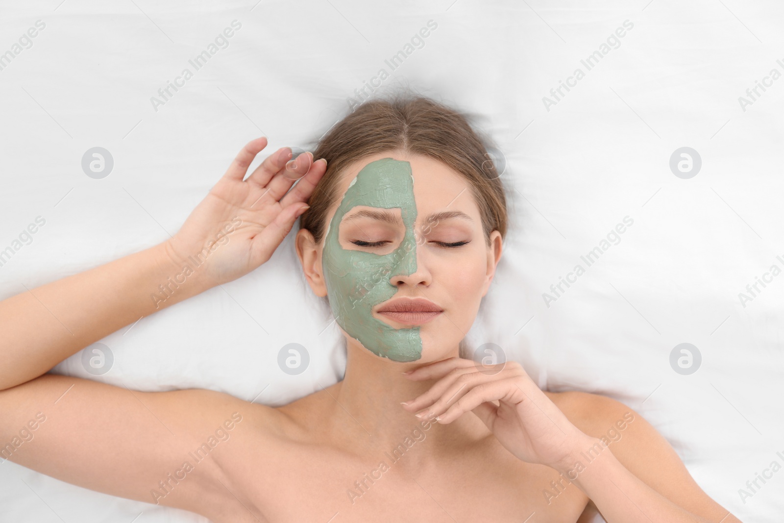 Photo of Beautiful woman with clay facial mask on white fabric, above view