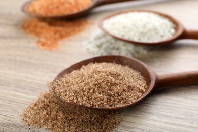 Spoons with different kinds of salt on wooden table, closeup