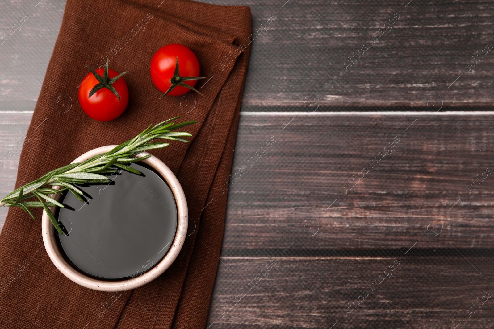 Photo of Bowl with balsamic vinegar, rosemary and tomatoes on wooden table, flat lay. Space for text