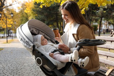 Happy mother with her baby daughter in stroller outdoors on autumn day