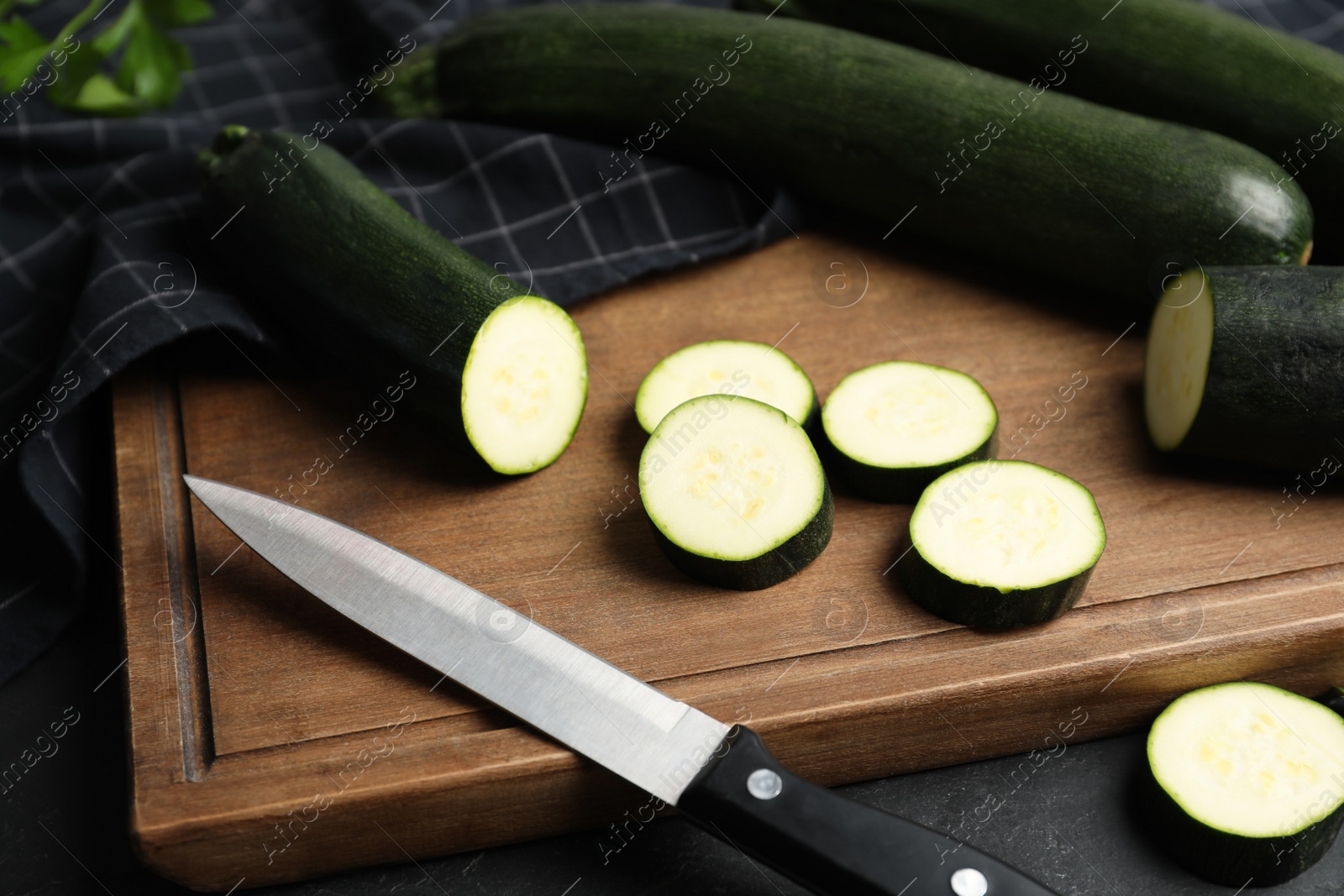 Photo of Green ripe zucchinis and wooden board on black slate table, closeup