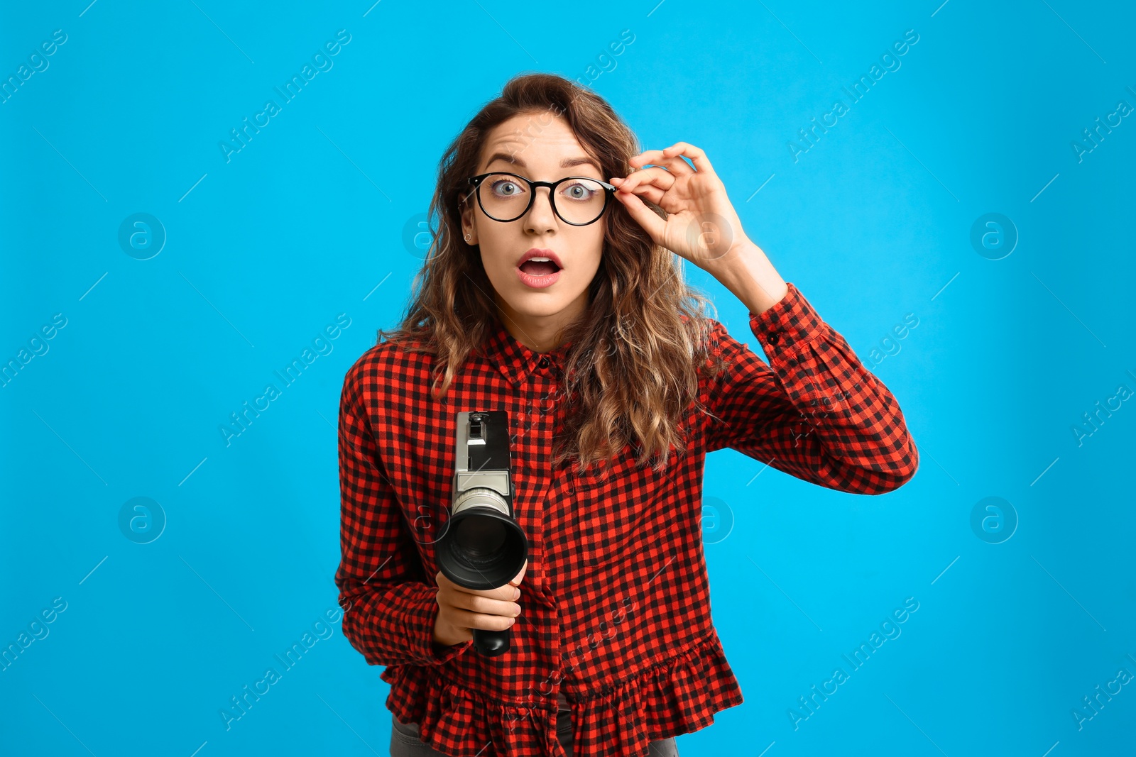 Photo of Beautiful young woman with vintage video camera on light blue background