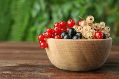 Photo of Different fresh ripe currants in bowl on wooden table outdoors, closeup. Space for text