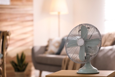 Photo of Modern electric fan on wooden table in living room. Space for text