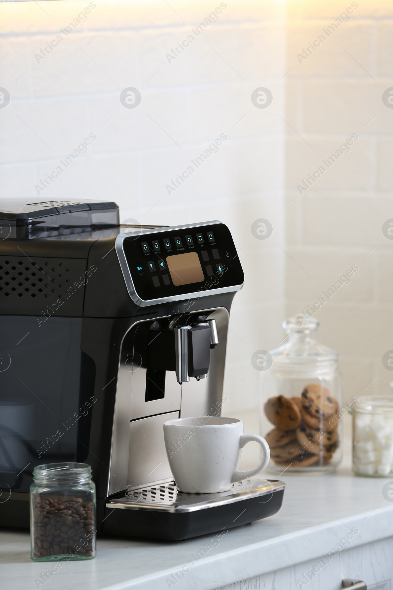 Photo of Modern electric coffee machine with cup on white countertop in kitchen