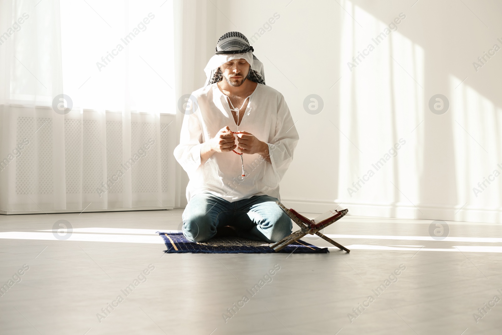 Photo of Muslim man in traditional clothes praying on rug indoors