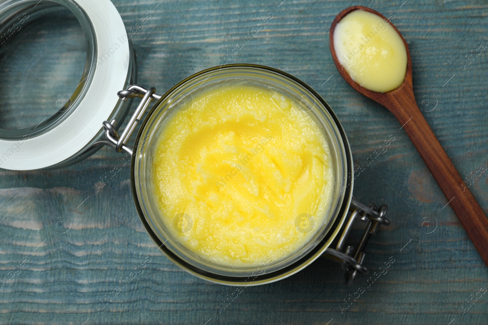 Photo of Glass jar and spoon of Ghee butter on light blue wooden table, flat lay