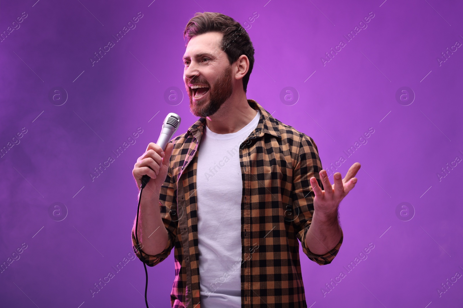 Photo of Handsome man with microphone singing on purple background