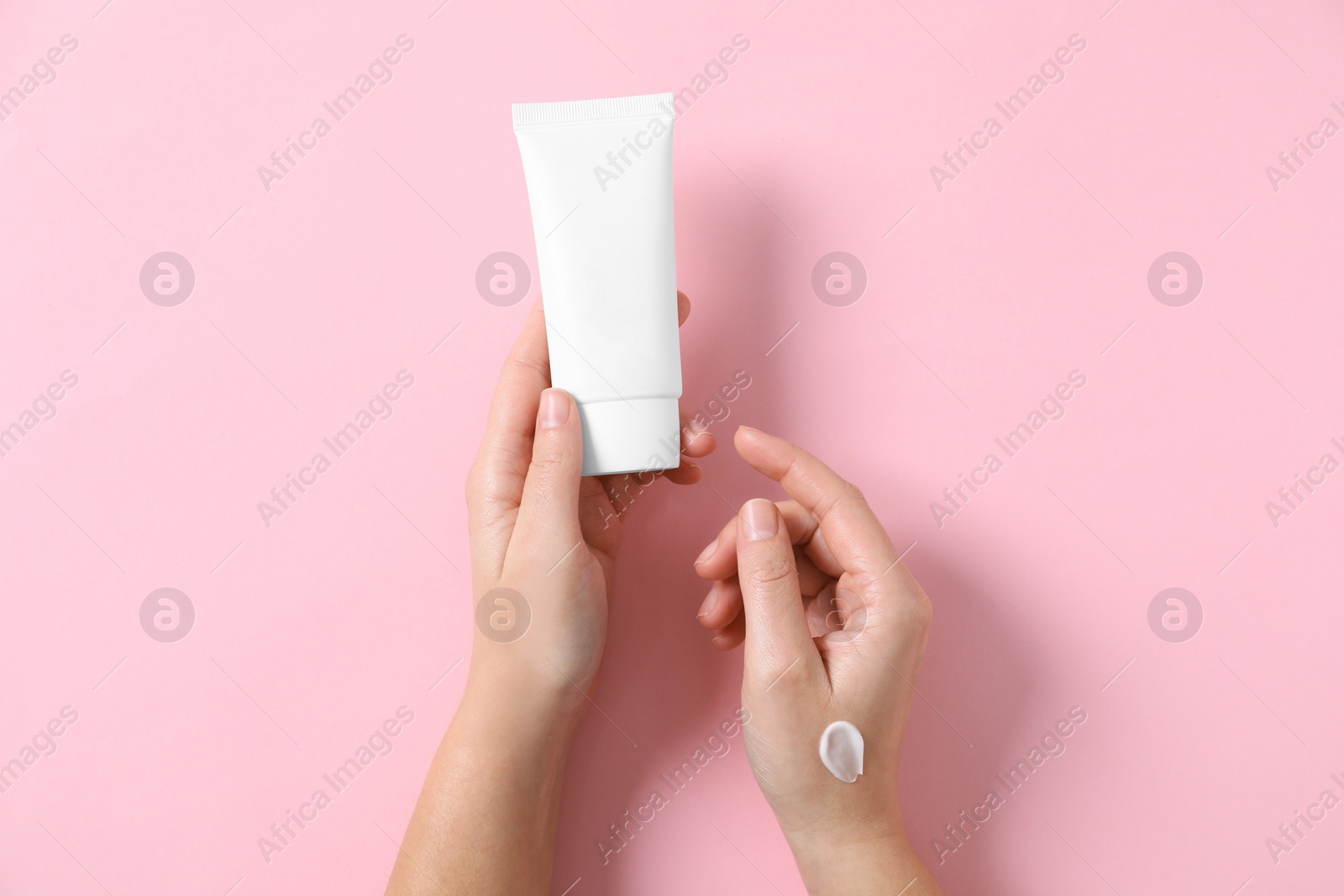 Photo of Woman with tube of hand cream on pink background, top view