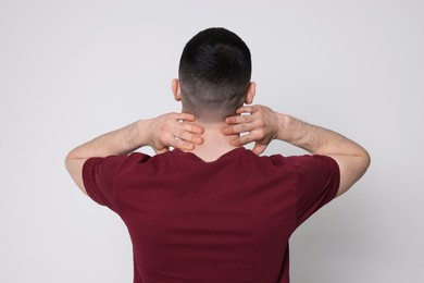 Photo of Man suffering from pain in his neck on light background, back view. Arthritis symptoms