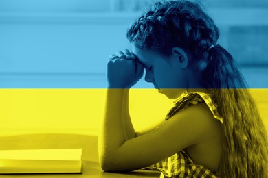 Image of Pray for Ukraine. Double exposure of little girl with Bible praying in room and Ukrainian national flag