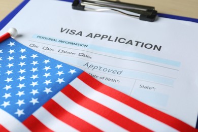 Photo of Visa application form for immigration and American flag on table, closeup