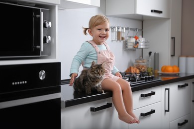 Photo of Cute little child sitting with adorable pet on countertop in kitchen