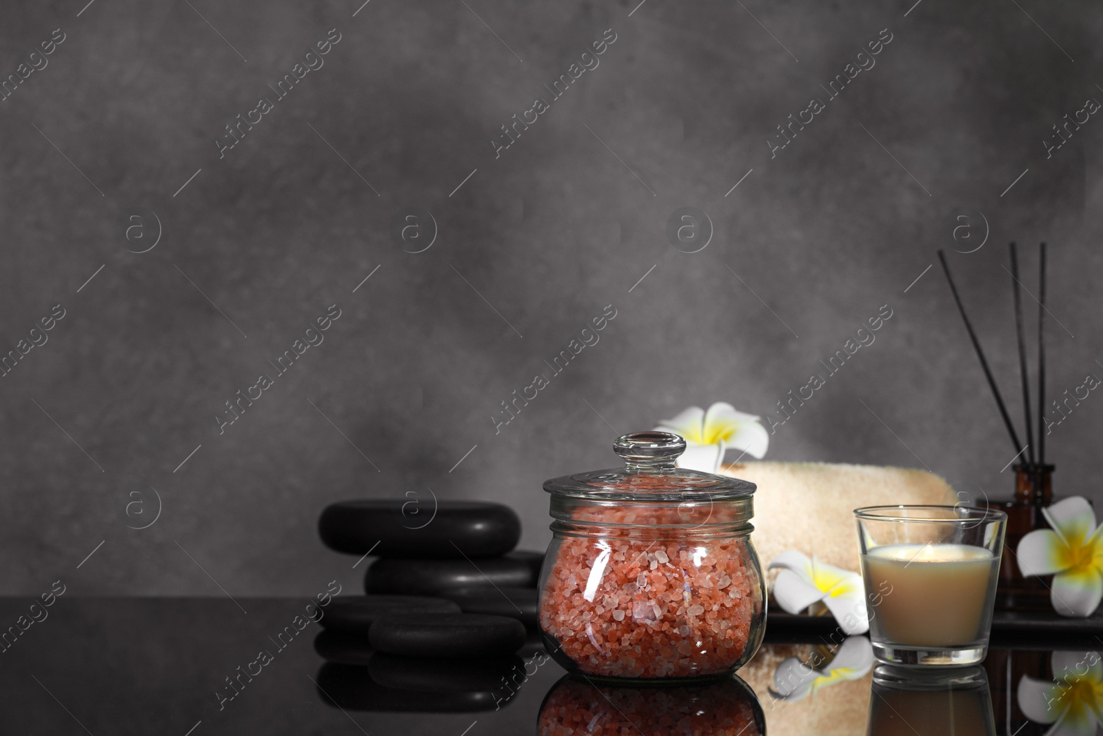 Photo of Glass jar with natural sea salt, beautiful flowers, candle and spa stones on mirror surface. Space for text