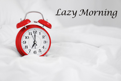 Image of Analog alarm clock on bed. Lazy morning