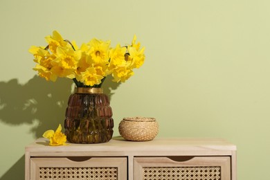 Beautiful daffodils in vase on table near light green wall, space for text