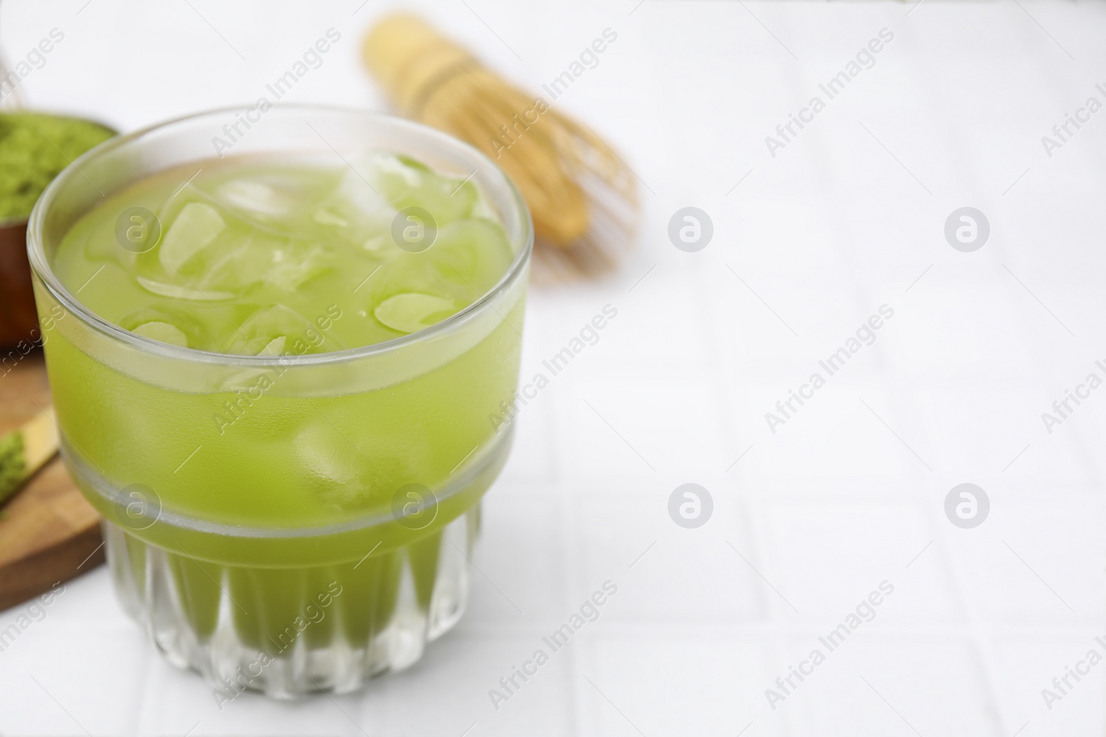 Photo of Glass of delicious iced green matcha tea on white tiled table, closeup. Space for text