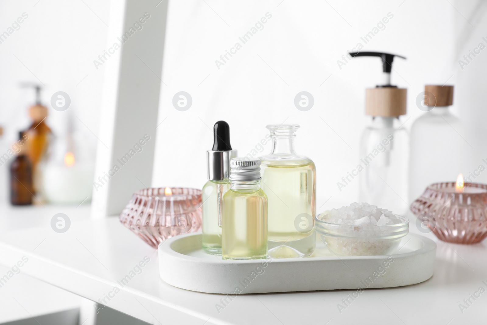 Photo of Essential oils, candles and sea salt on white shelf in bathroom