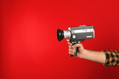 Man with vintage video camera on red background, closeup of hand. Space for text