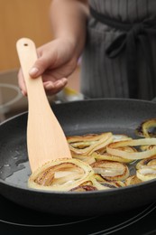 Woman cooking onion rings in frying pan on stove, closeup